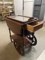 Side view of the antique wooden tea cart showing open drawer and glass tray on top, large wooden wheels, and turned legs.