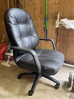 Photo showing black office desk chair with padded leather-like seat and backrest, armrests, and caster wheel base
