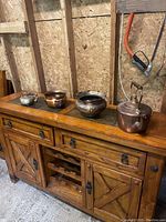 Four miscellaneous copper pots arranged on a wooden cabinet, showing variety in size and shape including a kettle and three pots.