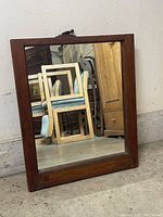 Photo of the wooden-framed rectangular mirror resting against a wall indoors, showing the dark stained wood frame and clear reflective mirror glass.