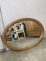 Oval mirror resting against a wall on a concrete floor with furniture reflected in the glass.
