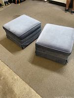 Two blue upholstered footrests positioned on carpeted floor showing intact fabric and casters underneath each footrest.
