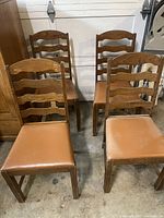 Four antique oak wooden chairs with ladder backs and tan cushioned seats arranged in two rows, showing overall structure and condition.