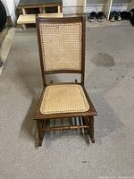 Front view of small wooden rocking chair showing woven rattan seat and backrest