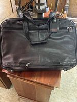 Front view of the black leather Tumi garment bag with handles and luggage tag