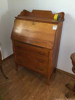Front view of solid oak antique secretary desk showing closed slant front and three drawers with metal handles.