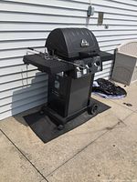 Full view of the black Sterling propane BBQ grill with rotisserie attachment on the side shelf and wheels on the base.