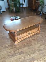 Front and side angle showing the coffee table's wood grain, drawer, turned legs, and lower shelf.