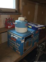 Original boxed Coleman Glacier Low Boy Snow-lite cooler with blue and white Coleman water jug on top and six-pack of Coca-Cola bottles in background
