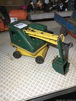 Side view of the vintage pressed steel excavator showing green cabin and yellow arm with bucket attachment.