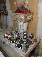 Overview of all garden critters and bird feeders on a bench showing red birdhouse feeder on box and multiple animal figurines in foreground.