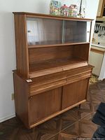 Front view of vintage Krug wood two-piece cabinet with hutch top featuring sliding glass doors and buffet base with drawers and doors.