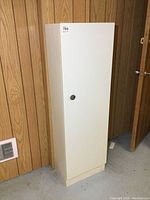 Front view of the tall, white, vintage metal pantry cabinet closed, showing the single door with a round handle.