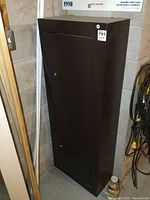 Tall brown metal cabinet shown closed from a side corner angle, measuring about 21x10x55 inches.