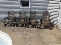 Four taupe brown resin rocking chairs lined up on concrete patio against siding
