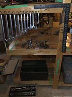 Wooden shelf displaying a row of large and smaller wrenches, Allen keys, sockets, and a metal toolbox on lower shelf