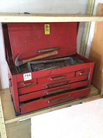 Front view of red metal toolbox with lid open showing hammer and various tools inside toolbox compartments and drawers.