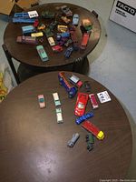 Various diecast toy vehicles arranged on two round wooden tables