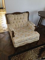 Angled view of vintage armchair showing tufted back, floral upholstery and wooden frame.