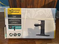 Factory sealed box showing front of the box with American Standard branding, model name Lez, and faucet image with features listed.