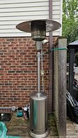 Full height view of the tall propane heater showing stainless steel base, vertical shaft and rusted heat shield.