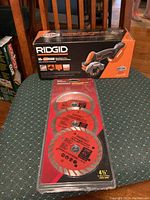 Ridgid 18V Sub Compact brushless multi-material saw box and three Benchmark 4.5 inch sealed saw blades in plastic blister pack on chair.