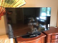 Front view of Samsung TV on pedestal stand with remote placed on base