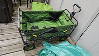 Soft side folding wagon with green fabric, black metal frame, and large wheels, shown open.