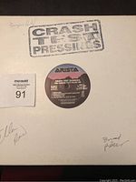 Front of the white vinyl sleeve with 'Crash Test Pressings' stamped in black and several signatures in pen.