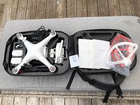 Open foam carrying case containing DJI Phantom 3 drone body, remote controller, two batteries, charger cable, user manual and propeller guards