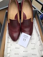 Pair of bordeaux Ecco women's leather slip-on shoes inside original box with branded tissue paper, size 41 EU tag visible.