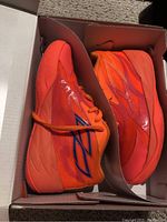 Pair of fiery coral and ultra orange Puma MB.02 Supernova PS kids shoes in original box, displayed sideview showing design and colors.