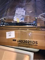 Photo showing the Lynk box labeled 20x21 Roll Out Cabinet Drawer and the drawer metal frame above it, covered partially with plastic.