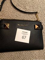 Close-up front of black Michael Kors purse showing gold pyramid studs and logo