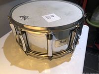 Pearl Session Elite snare drum in chrome finish with Remo Ambassador coated drum head placed on a white surface, showing the front side and hardware details.