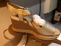 Single gold wedge sandal with cushioned footbed, ankle strap, and braided jute detail on wedge heel.