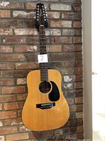 Full front view of Takamine 12-string guitar hanging against brick wall