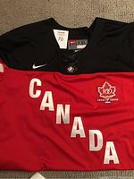 Front view of red and black Team Canada hockey jersey with 'CANADA' lettering and embroidered centennial logo showing size XXL Nike tag.