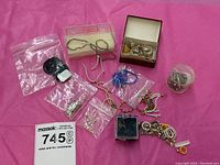 Overview of assorted doll jewelry pieces on pink background: zip bags, small box, jar, black bracelets, colorful beads.