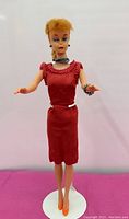 Full front view of Barbie on stand wearing red dress, jewelry and orange heels