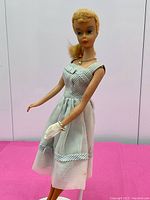 Full front view of Barbie doll standing on pink surface wearing striped Movie Date dress with glove and necklace visible