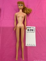 Full view of the blonde ponytail Barbie doll laid on pink fabric background without clothing showing overall condition.