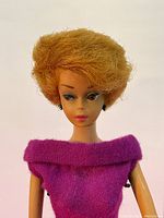 Close-up photo of Barbie's face and shoulders showing blonde Bubble Cut hair, earrings and magenta dress neckline.