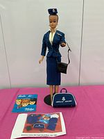 Full image showing Barbie in flight stewardess uniform with American Airlines travel bag and blue seating surface as background.