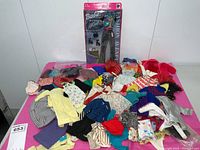 Photo showing a large assortment of vintage Barbie clothing laid out on a table including sweaters, dresses, coats, and other garments.