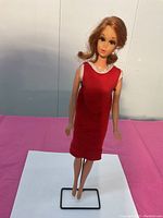 Photos of vintage Jamie Barbie doll posed on black metal doll stand wearing red dress with white collar trim. Doll marked on bottom approx 1970-72 Sears exclusive, Canada patent 1967.