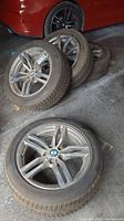 Four BMW alloy wheel and tire assemblies leaning against garage wall with red vehicle visible