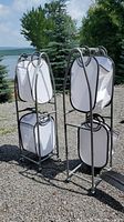 Photo showing two wheeled laundry carts with white hanging fabric bags outdoors on a gravel surface with trees and a lake in the background.