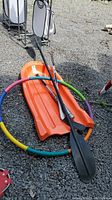 Orange plastic toboggan, black kayak paddle and colorful hula hoop arranged on gravel surface