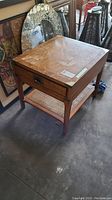 Full view of the wooden side table showing scratch marks, drawer, and rattan bottom shelf.